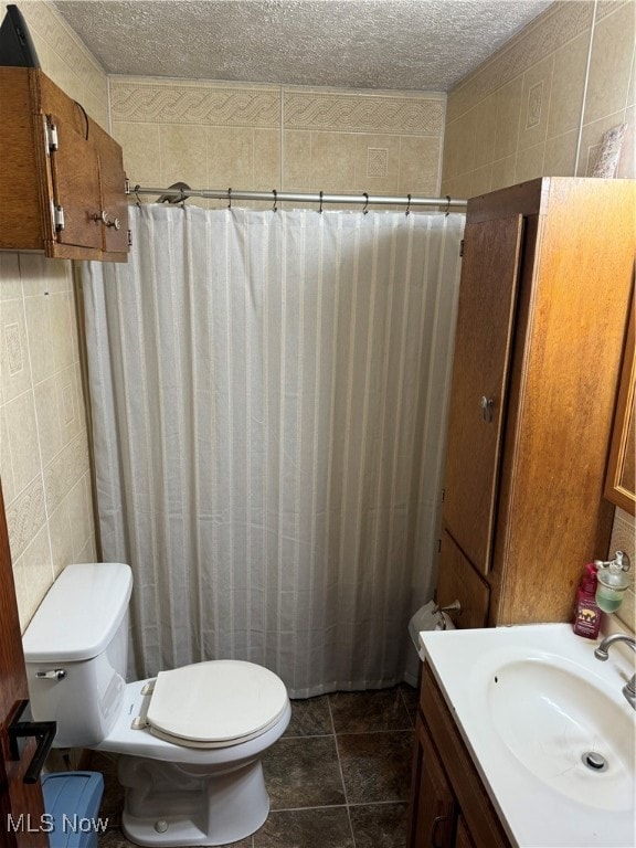 bathroom with vanity, a textured ceiling, tile patterned floors, tile walls, and toilet