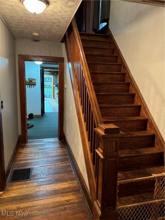 staircase with hardwood / wood-style floors and a textured ceiling