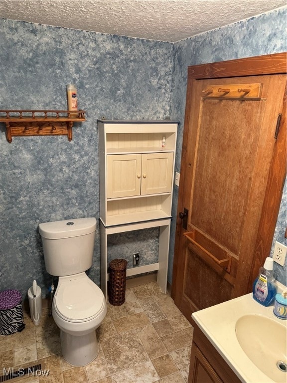 bathroom with a textured ceiling, vanity, and toilet