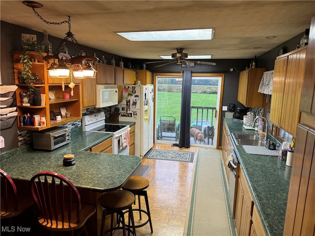 kitchen with a skylight, sink, white appliances, a breakfast bar area, and ceiling fan with notable chandelier