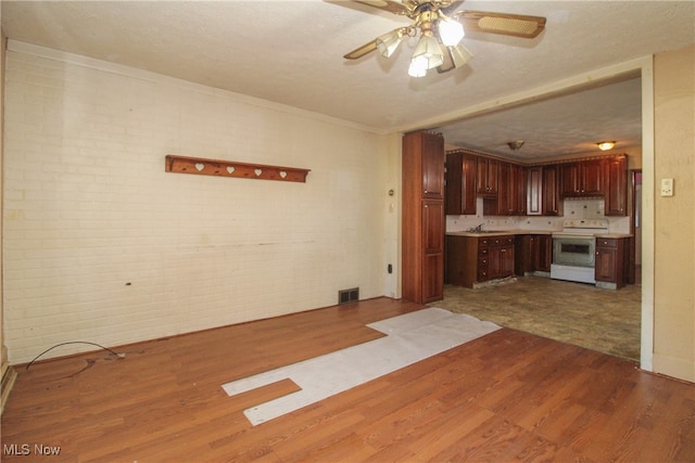 kitchen with ceiling fan, hardwood / wood-style floors, electric range, brick wall, and sink