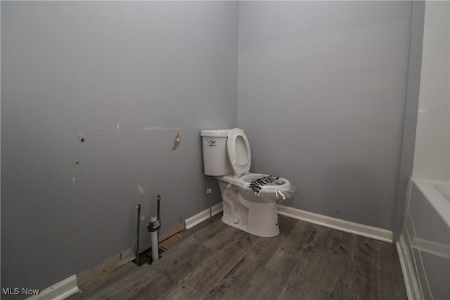 bathroom with hardwood / wood-style flooring, a bathing tub, and toilet