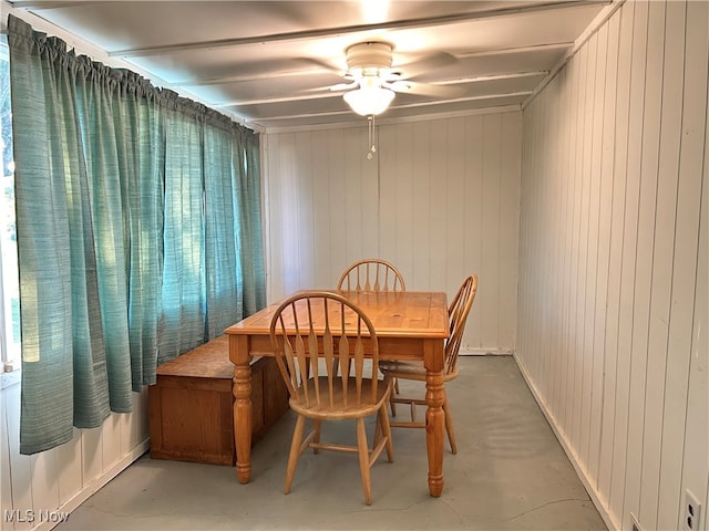 dining room featuring a healthy amount of sunlight, ceiling fan, wooden walls, and concrete flooring