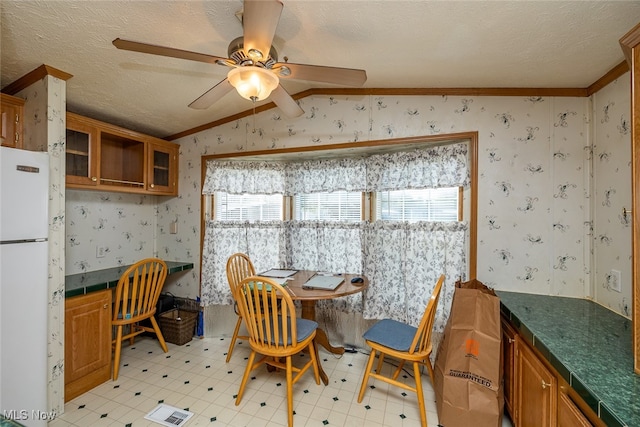 dining space with ceiling fan, ornamental molding, a textured ceiling, built in desk, and vaulted ceiling