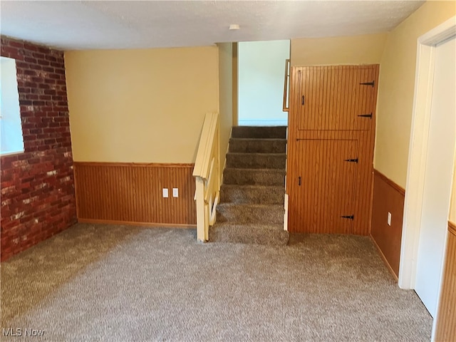 stairs featuring wooden walls, brick wall, and carpet flooring