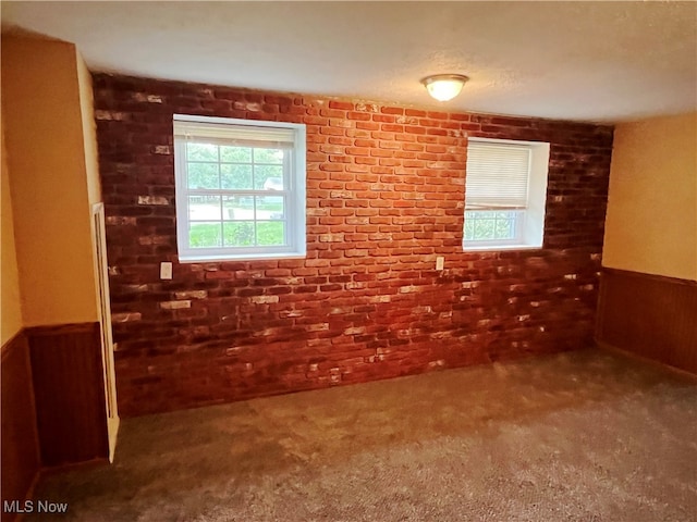 carpeted spare room featuring brick wall and wood walls