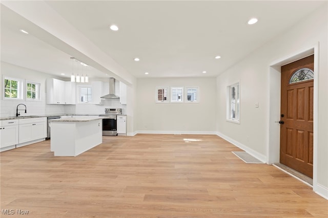 kitchen with decorative light fixtures, wall chimney range hood, white cabinetry, stainless steel appliances, and a center island