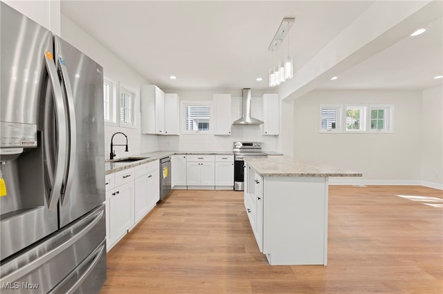 kitchen featuring a center island, white cabinets, sink, wall chimney range hood, and appliances with stainless steel finishes