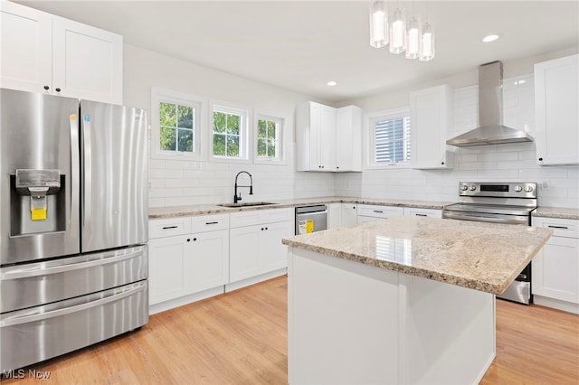 kitchen with a center island, stainless steel appliances, white cabinets, wall chimney exhaust hood, and sink