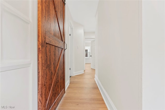 corridor with light wood-type flooring and a barn door