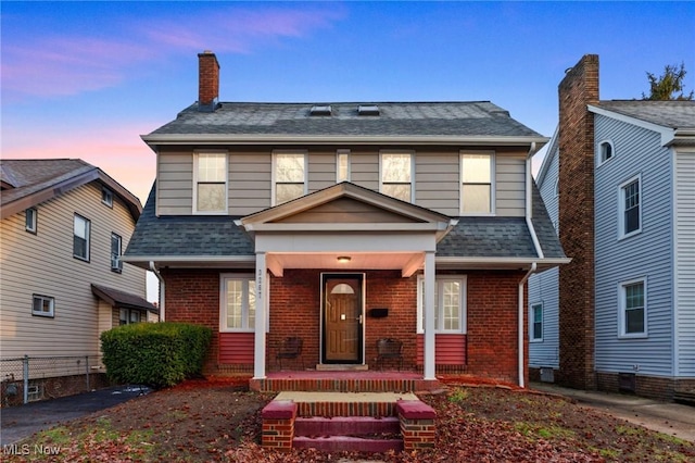 view of front of property featuring covered porch, brick siding, and a shingled roof