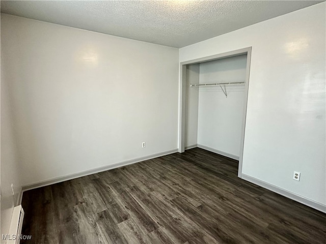 unfurnished bedroom featuring a textured ceiling, dark wood-type flooring, a closet, and baseboard heating