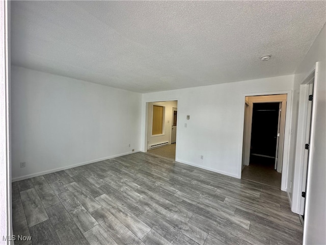 unfurnished room featuring hardwood / wood-style flooring, baseboard heating, and a textured ceiling