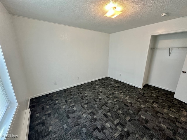 unfurnished bedroom with dark colored carpet, a closet, a baseboard heating unit, and a textured ceiling