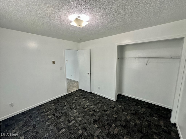 unfurnished bedroom with a closet, dark carpet, and a textured ceiling