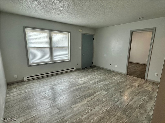 spare room with light hardwood / wood-style floors, baseboard heating, and a textured ceiling