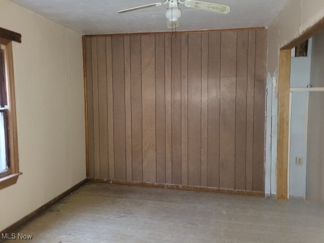 empty room featuring ceiling fan and wood walls