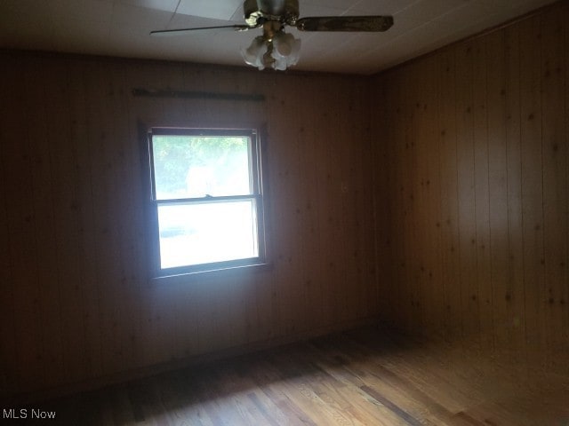 empty room with wood walls, hardwood / wood-style flooring, and ceiling fan