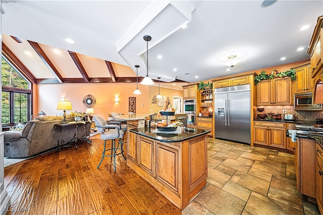 kitchen featuring a kitchen bar, a center island with sink, built in appliances, hanging light fixtures, and lofted ceiling with beams