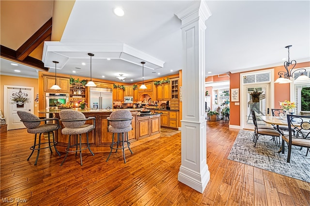 kitchen with light wood-type flooring, appliances with stainless steel finishes, hanging light fixtures, and decorative columns