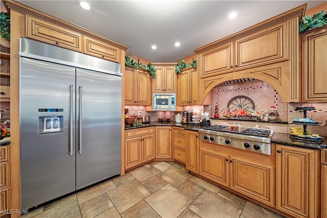 kitchen with dark stone countertops, decorative backsplash, custom range hood, and built in appliances