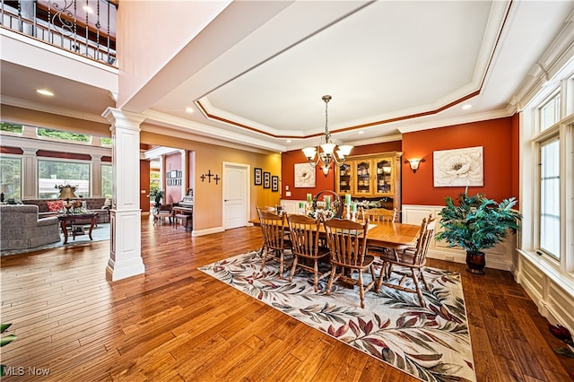 dining space featuring wood-type flooring, a raised ceiling, and decorative columns