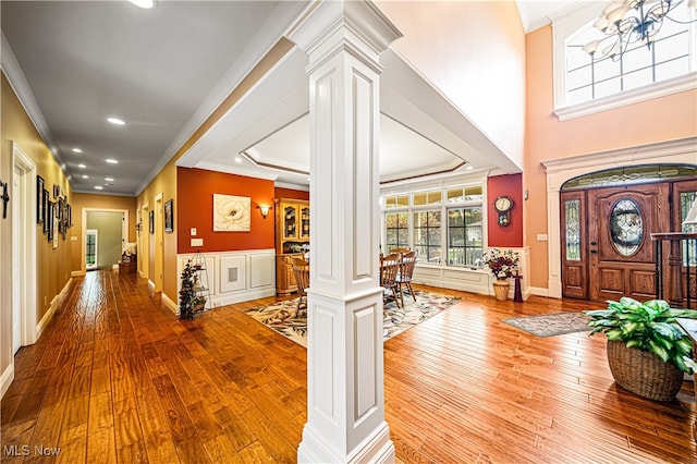 foyer featuring a notable chandelier, hardwood / wood-style flooring, decorative columns, ornamental molding, and a raised ceiling