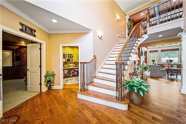 staircase with ornamental molding, hardwood / wood-style floors, and decorative columns