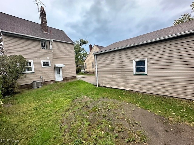 rear view of property with central AC unit and a lawn