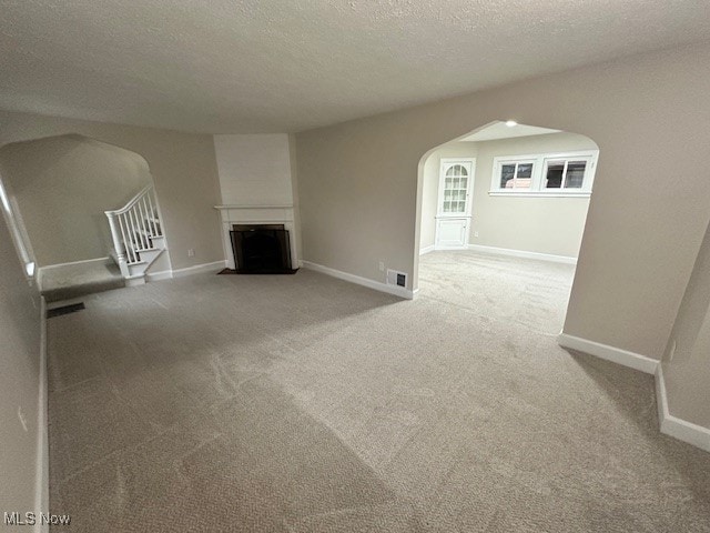 unfurnished living room with carpet floors, a large fireplace, and a textured ceiling