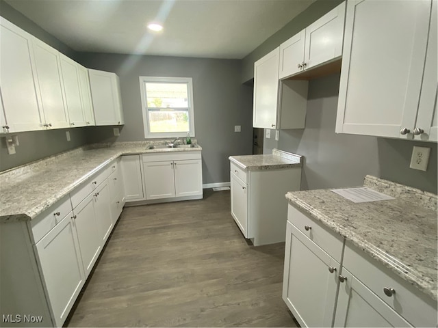 kitchen with light stone countertops, dark hardwood / wood-style floors, sink, and white cabinetry