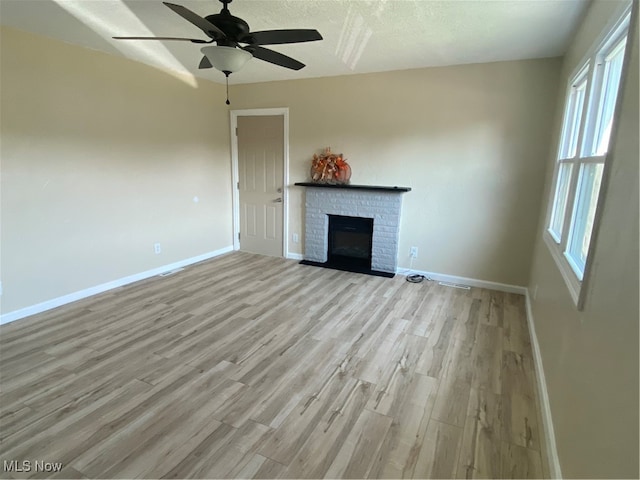 unfurnished living room with a brick fireplace, light hardwood / wood-style floors, a textured ceiling, and ceiling fan