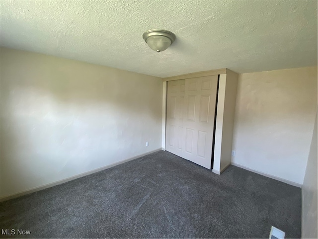 unfurnished bedroom with a closet, dark carpet, and a textured ceiling