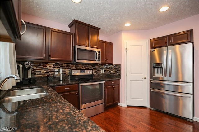 kitchen featuring tasteful backsplash, dark stone countertops, dark wood-type flooring, sink, and appliances with stainless steel finishes