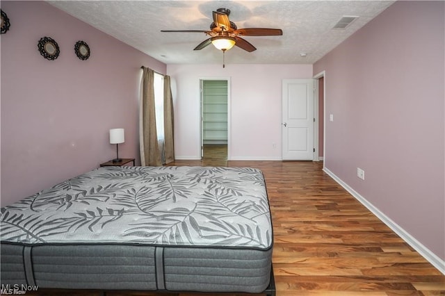 bedroom featuring wood-type flooring, a walk in closet, a textured ceiling, and ceiling fan