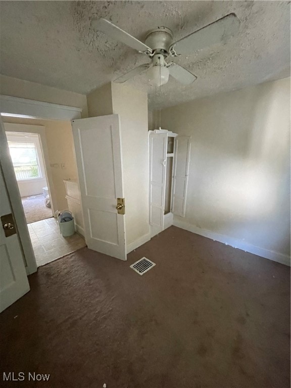 unfurnished bedroom with ceiling fan, dark carpet, and a textured ceiling