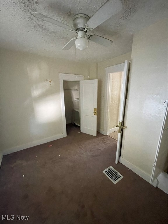 unfurnished bedroom featuring ceiling fan, dark carpet, and a textured ceiling