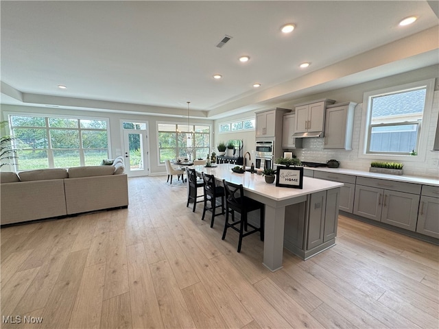 kitchen with a breakfast bar area, an island with sink, backsplash, light wood-type flooring, and gray cabinets