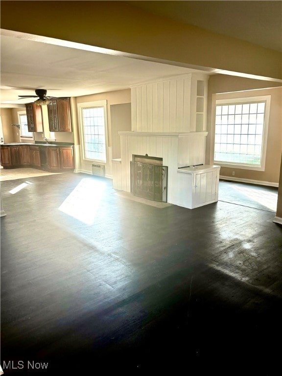 unfurnished living room featuring a large fireplace, dark hardwood / wood-style flooring, and a healthy amount of sunlight