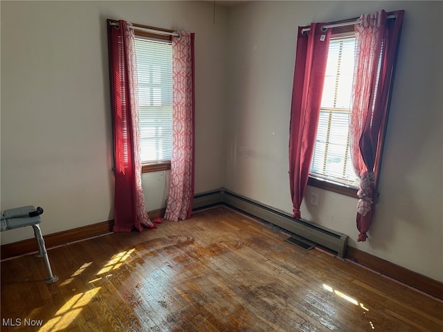 spare room featuring baseboard heating, plenty of natural light, and hardwood / wood-style floors