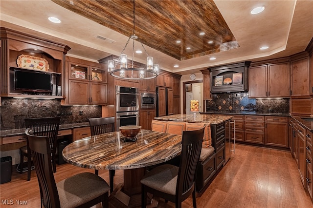 kitchen featuring built in appliances, dark stone countertops, a tray ceiling, a kitchen island, and dark wood-type flooring