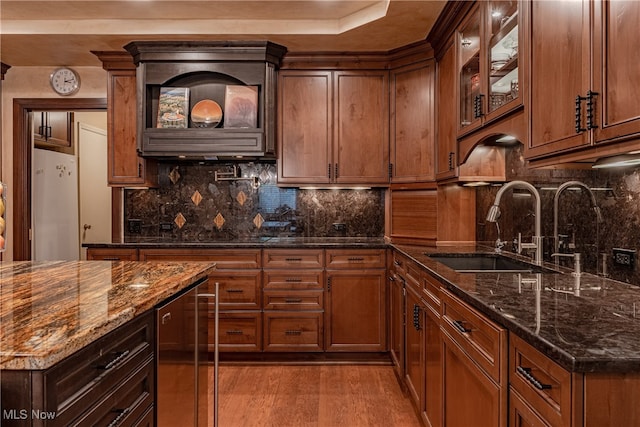 kitchen with light hardwood / wood-style floors, white refrigerator, sink, backsplash, and dark stone countertops