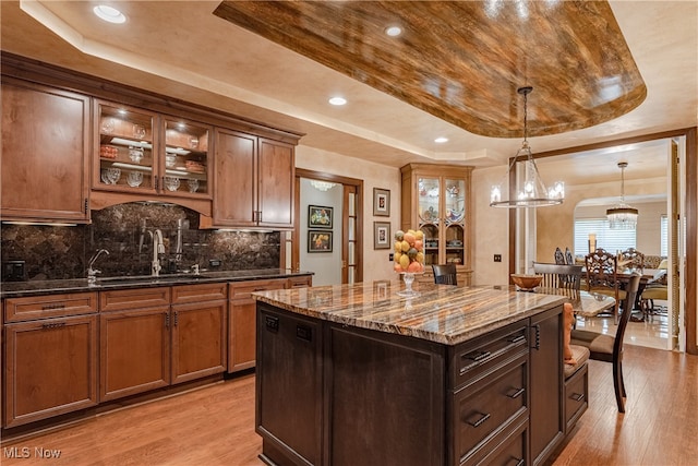 kitchen with dark stone counters, light wood-type flooring, a kitchen island, and a tray ceiling