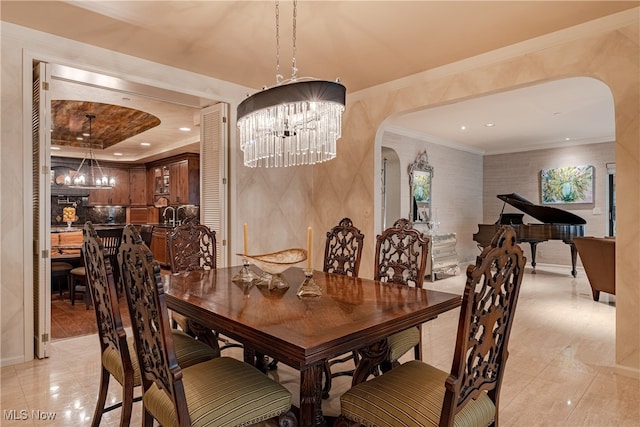 dining area with sink, a notable chandelier, ornamental molding, and a raised ceiling