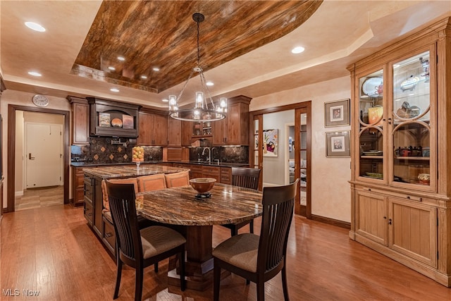 dining space with hardwood / wood-style floors, sink, an inviting chandelier, and a tray ceiling