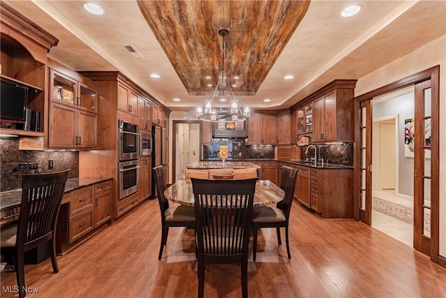 kitchen with light wood-type flooring, hanging light fixtures, a raised ceiling, and dark stone countertops