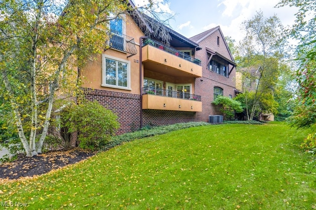 rear view of house with a balcony, a lawn, and central AC unit