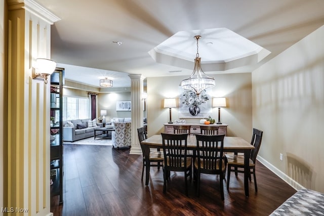 dining room featuring ornamental molding, a chandelier, dark wood-type flooring, a tray ceiling, and ornate columns