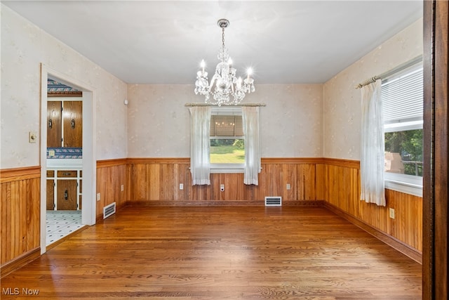 unfurnished dining area with a notable chandelier, hardwood / wood-style floors, and a wealth of natural light