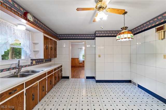 kitchen featuring ceiling fan, hanging light fixtures, sink, and tile walls